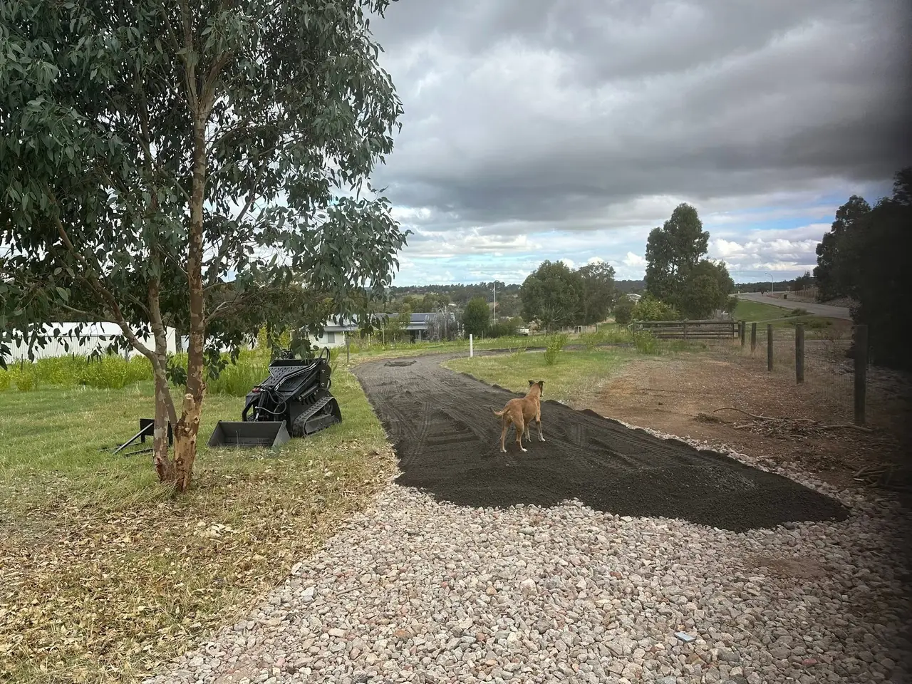 Recycled asphalt going down on a rural driveway, mini loader and the site dog on it