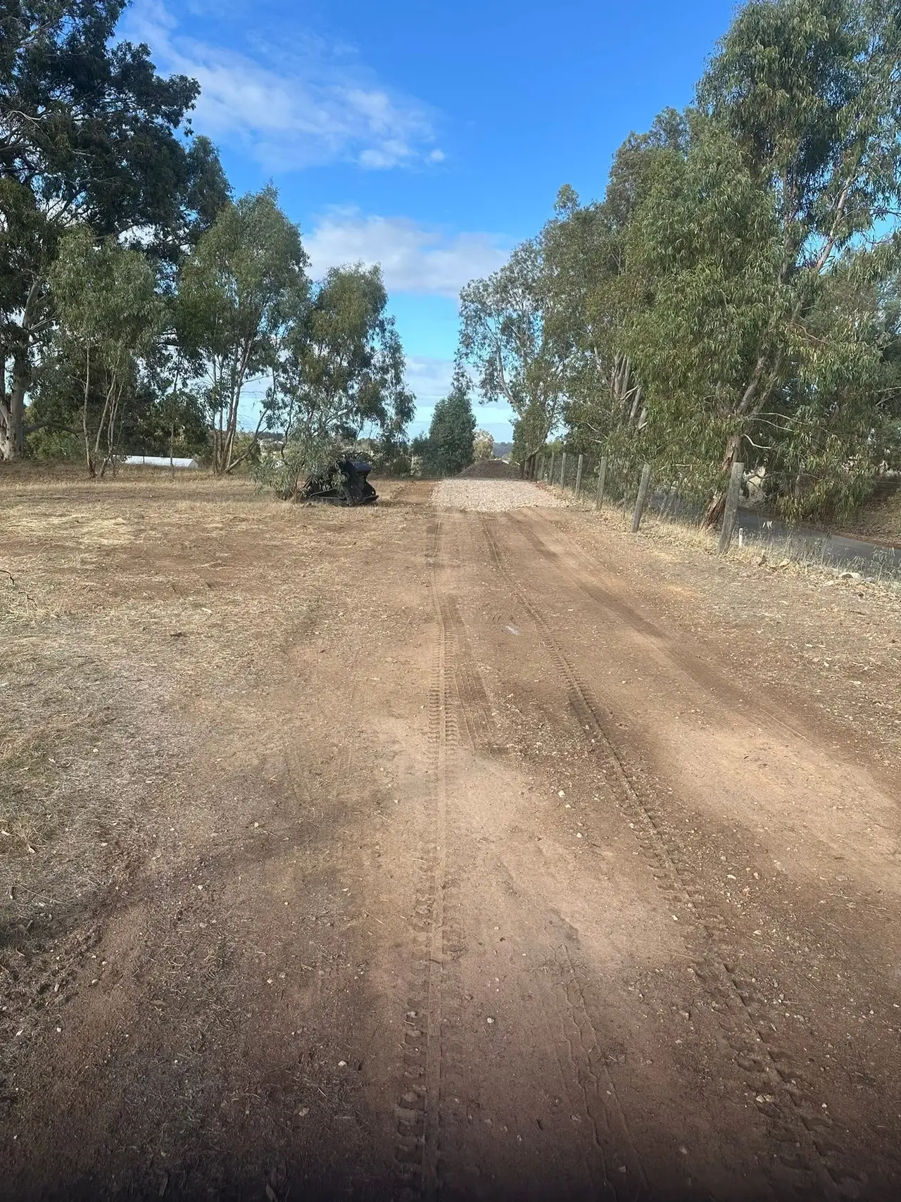 Long rural driveway cut in and graded flat, mini loader at the far end